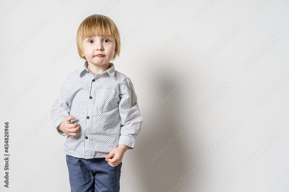 Half length portrait of small blonde caucasian boy standing in front of white wall looking to the side - little child studio portrait with copy space Half length portrait of small blonde caucasian boy standing in front of white wall looking to the side - little child studio portrait with copy space