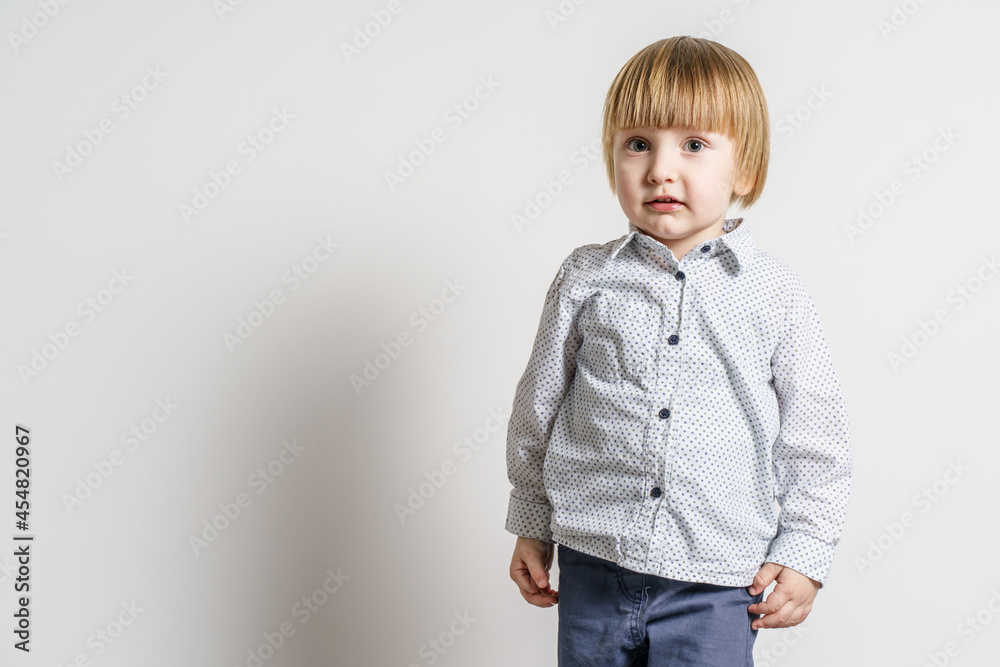 Half length portrait of small blonde caucasian boy standing in front of white wall looking to the side - little child studio portrait with copy space Half length portrait of small blonde caucasian boy standing in front of white wall looking to the side - little child studio portrait with copy space