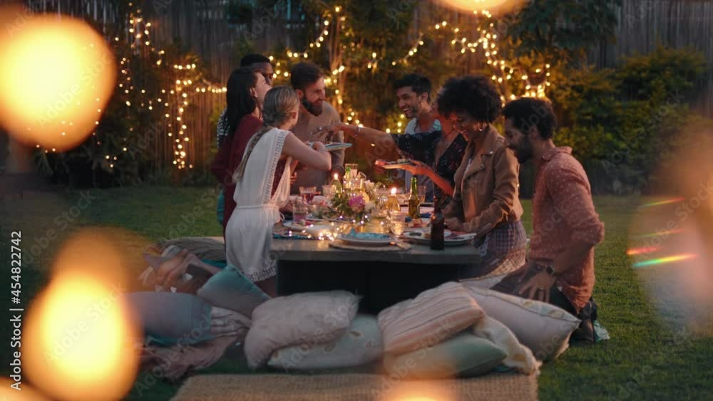 young group of friends celebrating at dinner party chatting sharing healthy food sitting at table enjoying weekend reunion relaxing on beautiful summer evening outdoors 4k