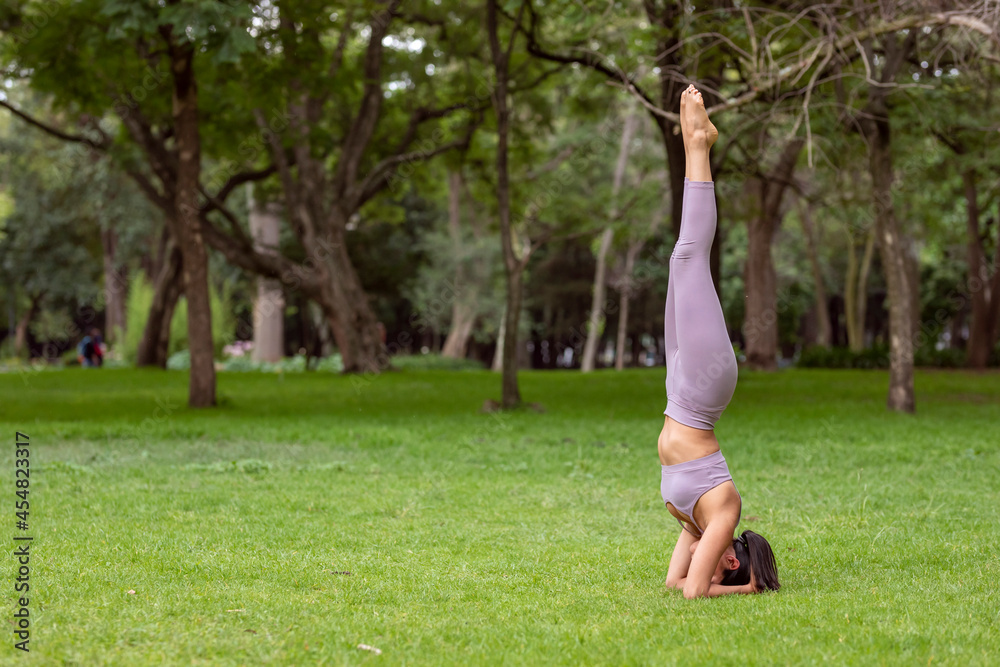 Woman doing yoga asanas in the park on the grass with trees in the background.