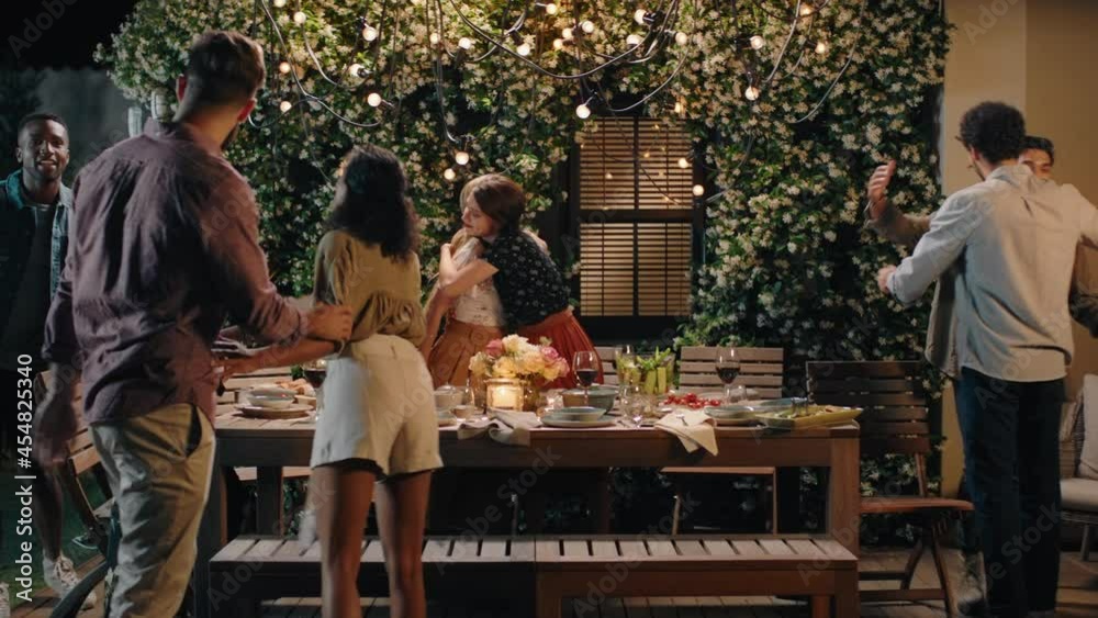 happy friends arriving at dinner party celebration hugging enjoying friendship reunion gathering sitting at table with healthy food sharing weekend together on beautiful summer night 4k