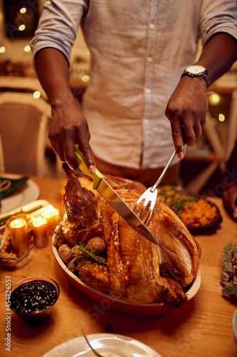Close-up of black man carves turkey meat during Thanksgiving meat at dining table.