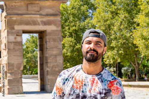 Young man with beard and cap pulled back looking seriously