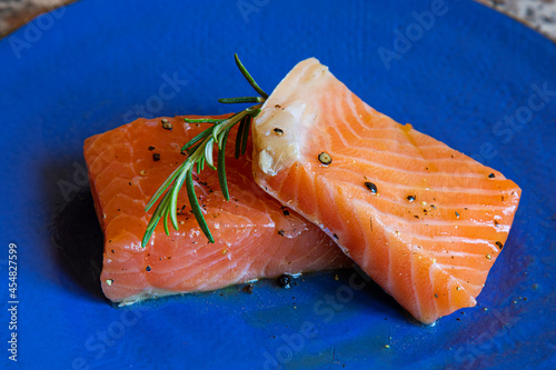 pieces of pickled salmon garnished with sage and rosemary leaves on a blue plate on a marble background