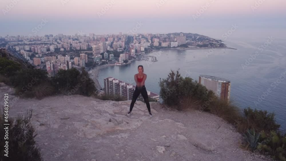Video 4K de deportista haciendo swing con kettlebell, en la montaña, con vistas al mar y a la ciudad.