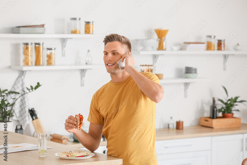 Handsome young man talking by phone while eating tasty quesadilla at home Handsome young man talking by phone while eating tasty quesadilla at home