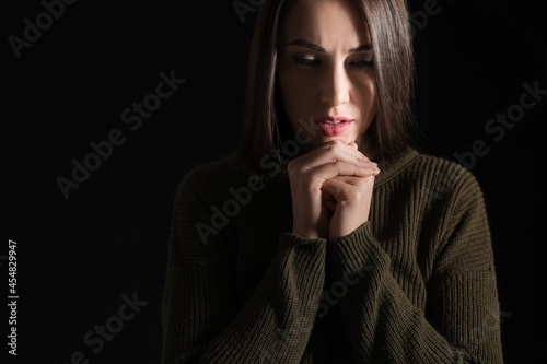 Praying young woman on dark...