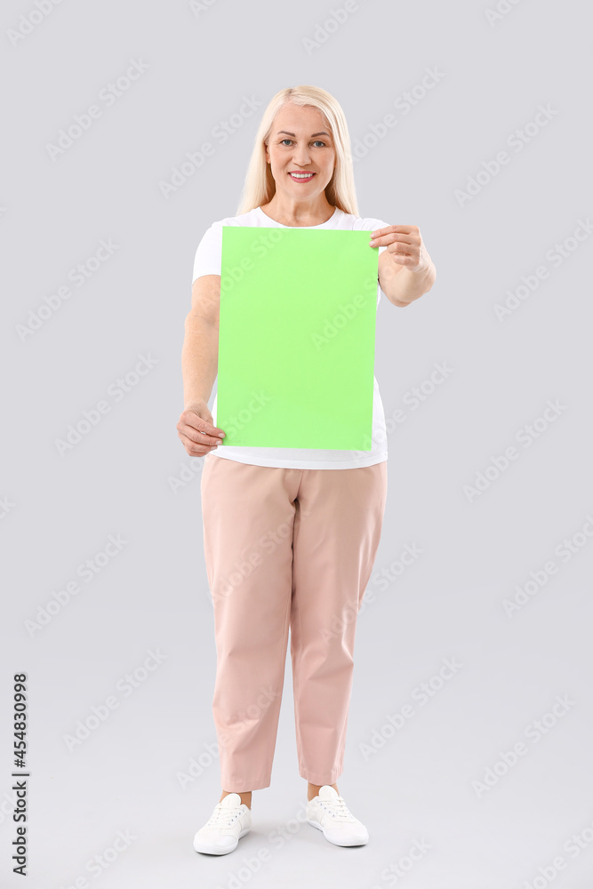 Mature woman with blank paper sheet on light background Mature woman with blank paper sheet on light background