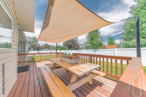 Deck of a house with wooden chairs and table under a shade sail