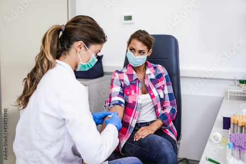 Nurse taking blood sample from young female patient in the background. Selective focus on sample tube.