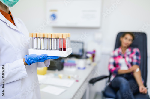 Nurse holding blood sample tubes. from young female patient in the background. Selective focus on sample tubes.