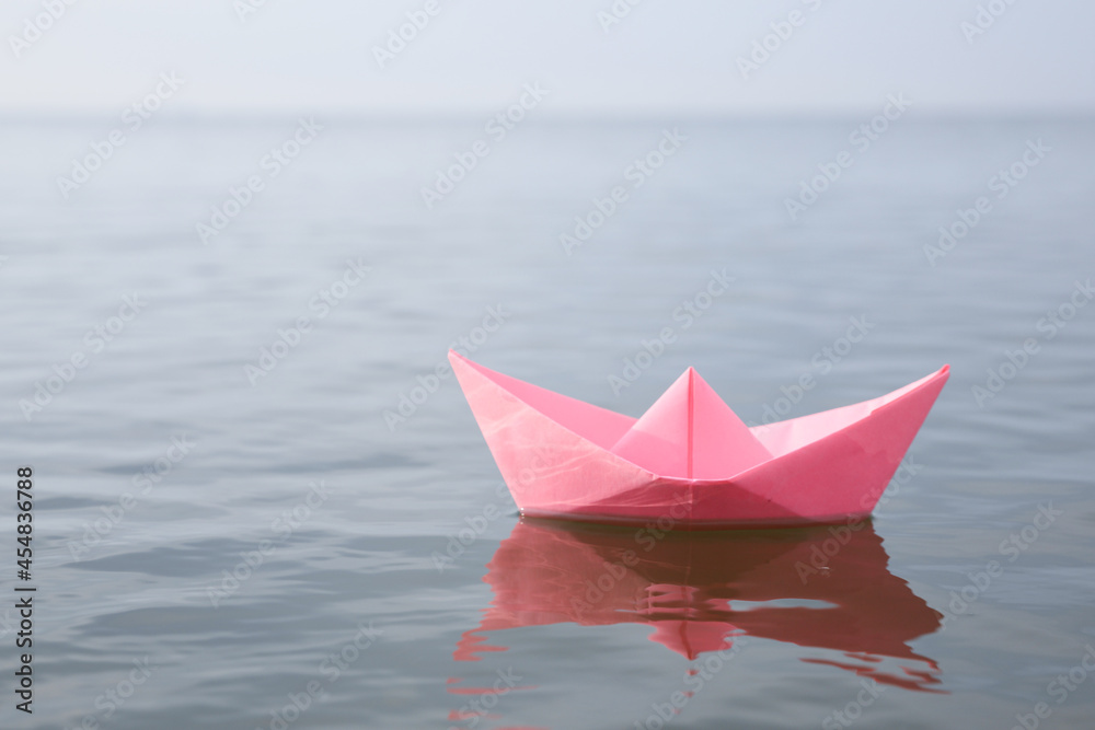 Pink paper boat on water surface, space for text