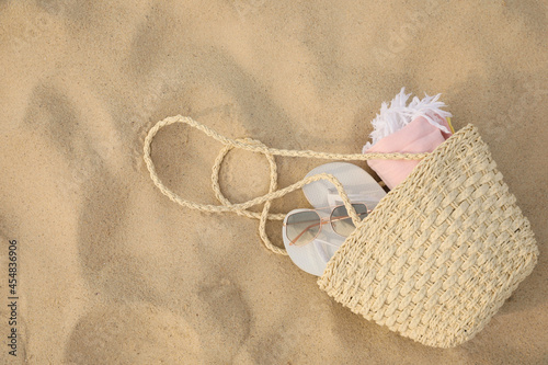 Beach bag with flip flops, towel and sunglasses on sand, top view. Space for text