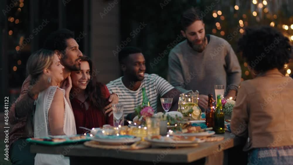 young group of friends celebrating at dinner party chatting sharing healthy food sitting at table enjoying weekend reunion relaxing on beautiful summer evening outdoors 4k
