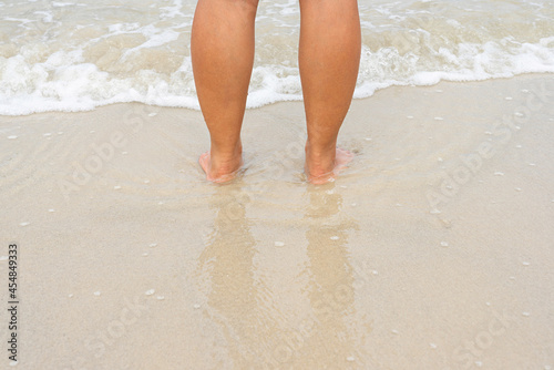 Asian female legs standing on wet sand beach