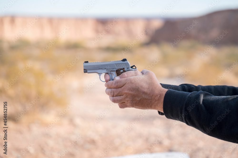 Hand of a man holding a small silver gun aiming on the left Hand of a man holding a small silver gun aiming on the left