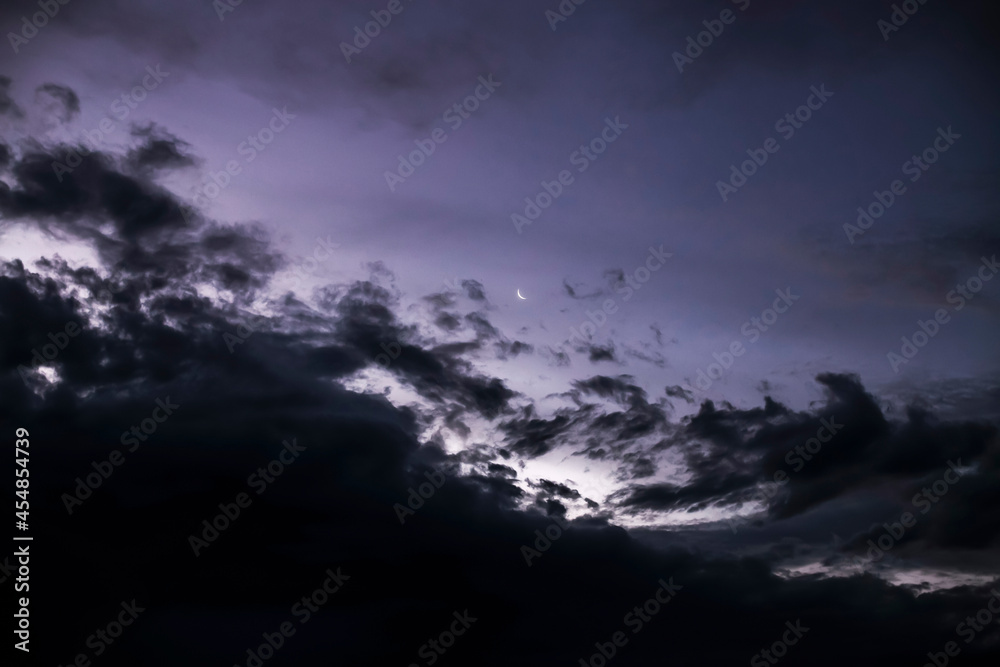 crescent moon in the distance in the night sky with dark stormy clouds coming in crescent moon in the distance in the night sky with dark stormy clouds coming in