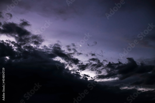 crescent moon in the distance in the night sky with dark stormy clouds coming in