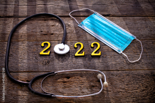 Stethoscope with 2022 number and medical mask on wooden  background. Happy New Year for health care . Сopy space.