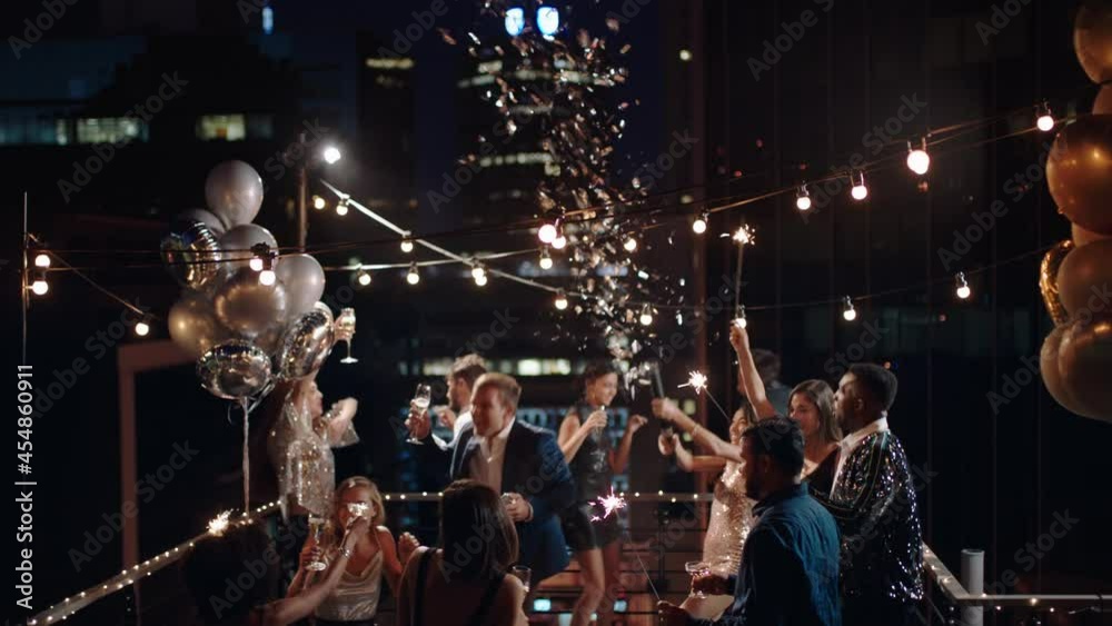 friends celebrating new years eve party dancing throwing confetti enjoying glamorous celebration wearing stylish fashion at formal social gathering on rooftop at night 4k 
