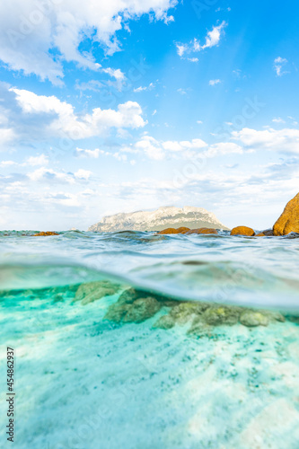 (Selective focus) Split-shot, over-under shot, half in half out. Crystal clear, turquoise water in the foreground and Tavolara Island in the distance. Sardinia, Italy.