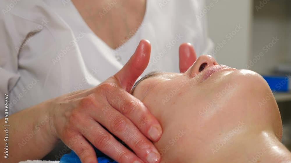 Wellness and beauty salon. Beautician making cure procedures on female client face in modern cosmetology clinic. Cosmetologist doctor making myoplastic anti-aging facial massage. 4 k video Wellness and beauty salon. Beautician making cure procedures on female client face in modern cosmetology clinic. Cosmetologist doctor making myoplastic anti-aging facial massage. 4 k video