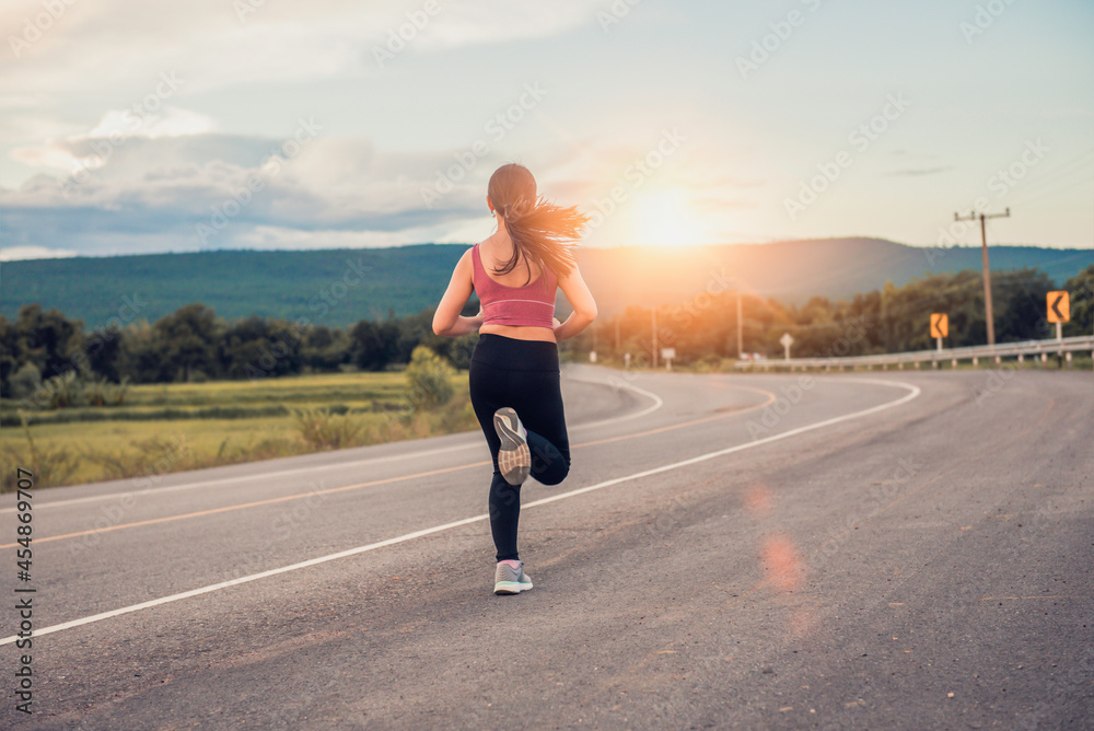 Young woman runner running on city road with mountains in the background.