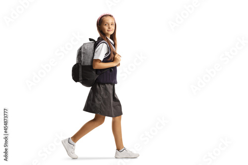 Full length shot of a schoolgirl in a uniform carrying a backpack and walking while looking at camera