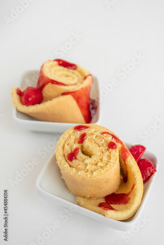Biscuit roll with strawberry jam on the white plate on white background.