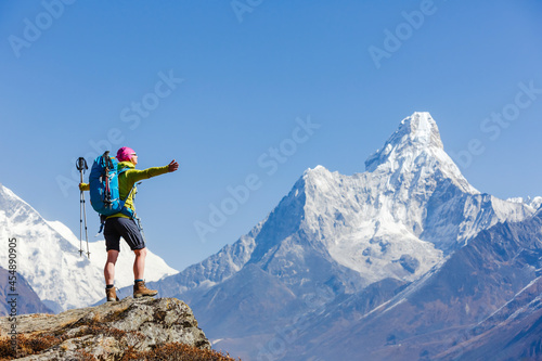Young female hiker with backpack relaxing on top of a mountain during sunny summer day