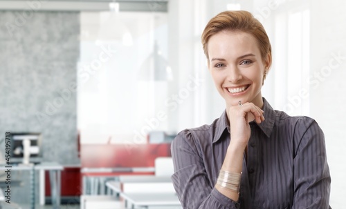 Confident young white businesswoman smiling in modern business office. Portrait of adult woman in 20s, happy confident smile. Copy space.