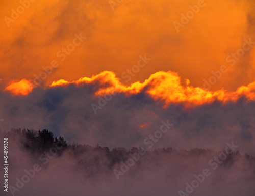 Dramatic scene including fiery sunrise on extremely cold winter morning with sea fog and clouds appearing as if in flame or as ablaze and sun barely visible trough clouds / sea smoke.