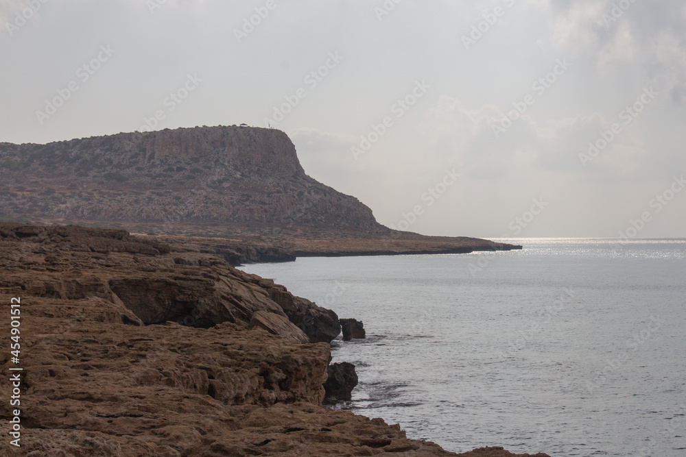Rocky coastline with mountain on background around Cape Greco, Cyprus.