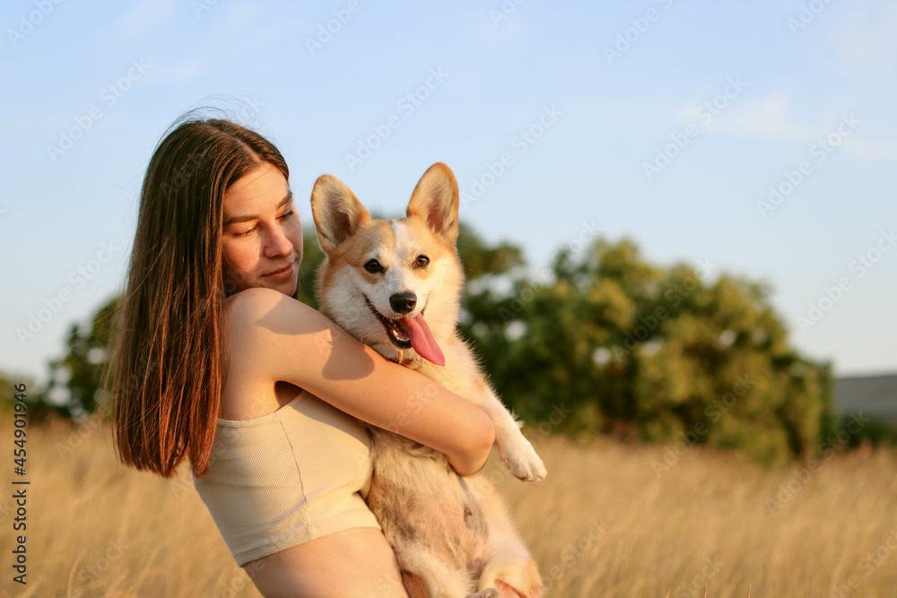 A contented happy girl holds a cute corgi dog, plays and lovingly hugs a corgi, walks with him in nature. People and dogs A contented happy girl holds a cute corgi dog, plays and lovingly hugs a corgi, walks with him in nature. People and dogs