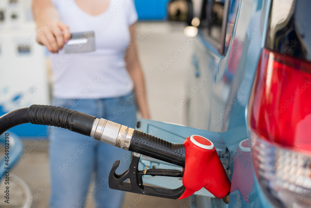 Fototapeta premium A woman fills her car with gasoline at a self-service gas station and holds a credit card