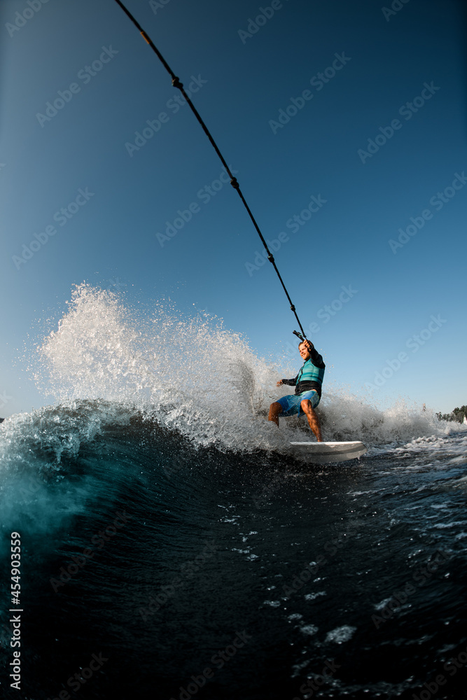 Naklejka premium man riding on the wakesurf holding rope of motorboat on the background of blue sky