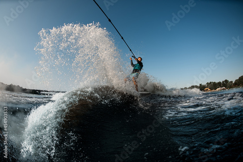 Active man riding on the wakesurf holding rope of motorboat on the background of blue sky © fesenko