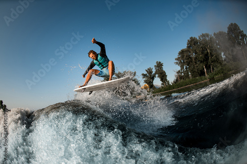 wakesurfer jumping on high wave of motorboat on the background of blue sky