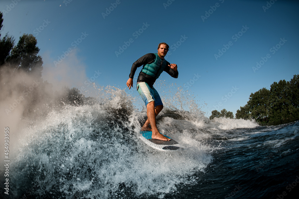 Active wakesurfer riding on wake board down the river waves against the blue sky