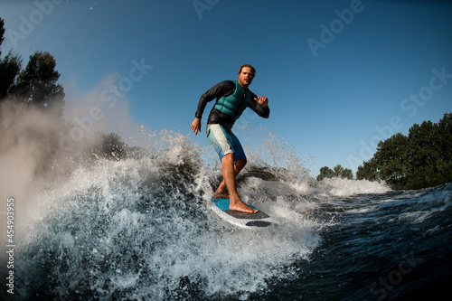 Active wakesurfer riding on wake board down the river waves against the blue sky