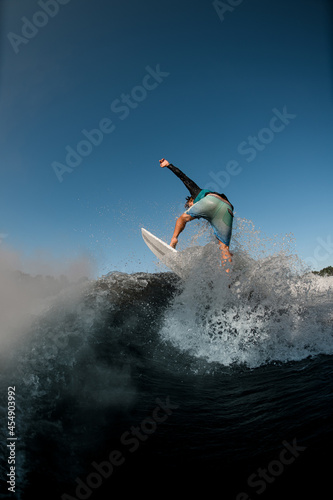 Wet man wakesurfer balances on splashing river wave against the blue sky