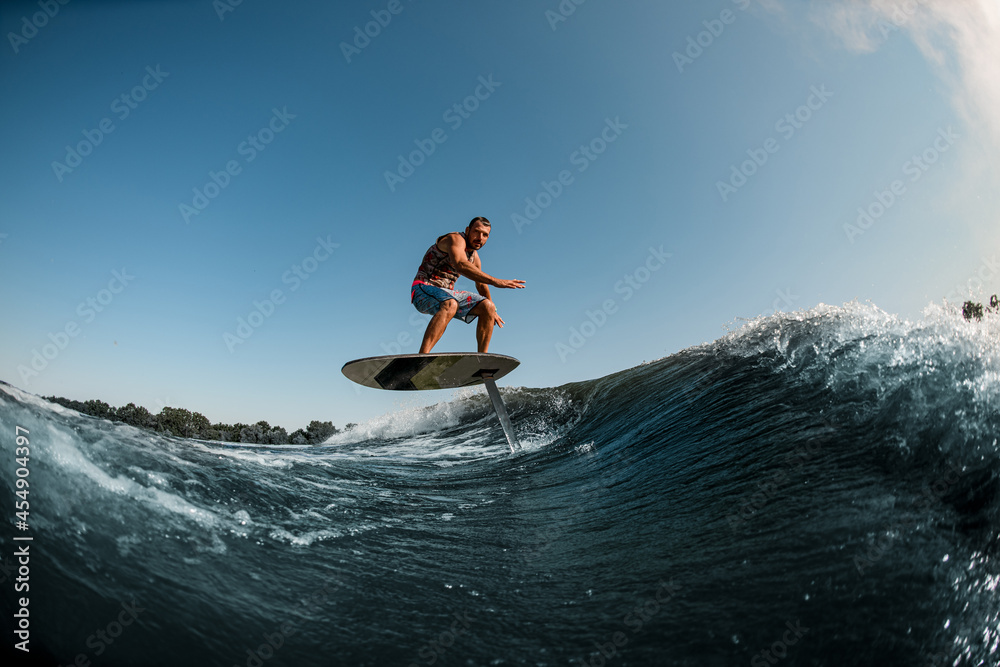 athletic man balancing on the wave with hydrofoil foilboard on background of blue sky