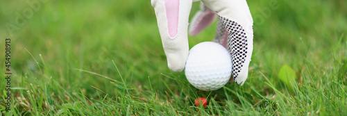 Hand in golf glove puts ball on golf tee