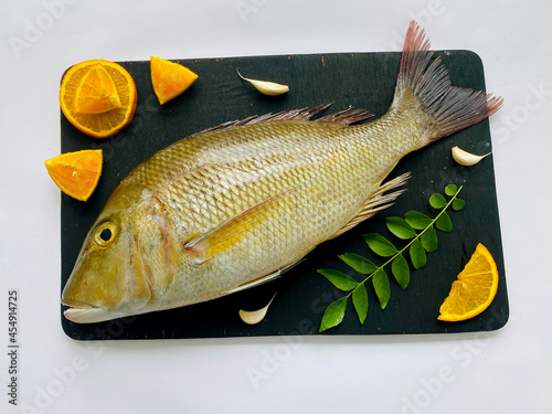 Fresh Emperor Fish decorated with herbs and vegetables on a black pad.White Background. photo