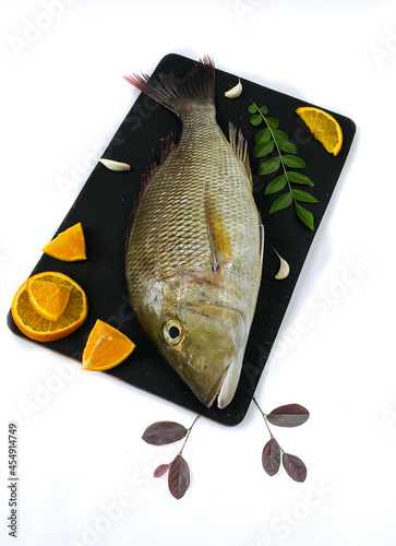 Fresh Emperor Fish decorated with herbs and vegetables on a black pad.White Background photo