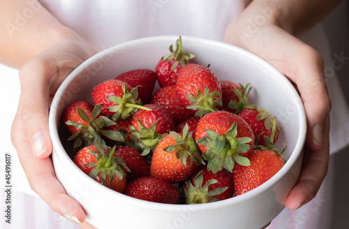 Young woman holding a white bowl with fresh strawberries. Close up of woman hands holding strawberries.