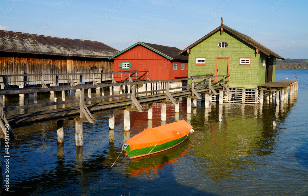 a long wooden pier leading to the colorful boat houses on lake Ammersee in the scenic German fishing village Schondorf (Germany)
