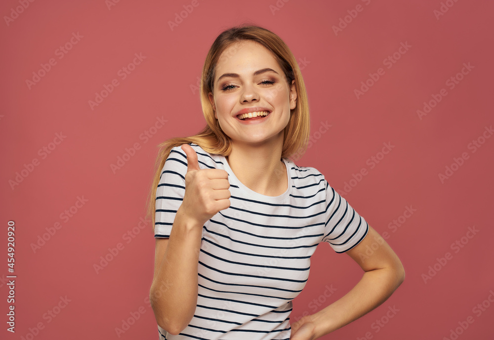blonde woman in a striped T-shirt fun hand gestures pink background blonde woman in a striped T-shirt fun hand gestures pink background