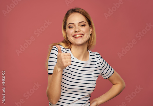 blonde woman in a striped T-shirt fun hand gestures pink background