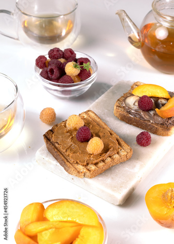 Healthy breakfast. Sandwiches or toasts with peanut butter  chocolate paste and yellow and red raspberries  blackberry on white table